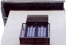 Rehabilitación de una fachada por la oficina de rehabilitación de Granada: alero marrón oscuro, Carpinterías y persianas de madera marrón oscuro y solera tradicional con losetas en su color.